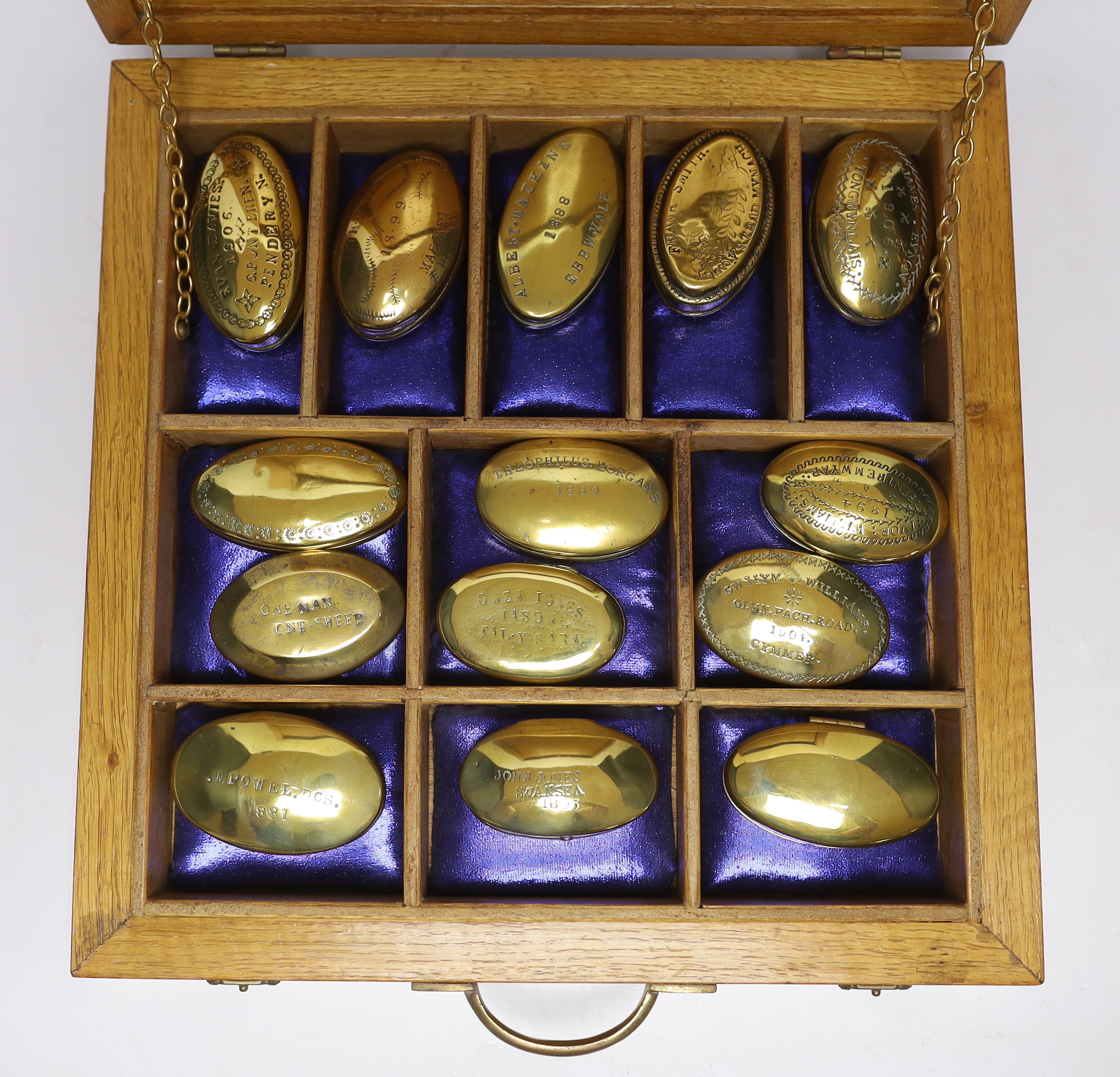 A collection of late 19th and early 20th century Welsh and English miner’s oval brass snuff boxes, most engraved with owner’s name and date, in a sectional oak box, largest snuff box 8cm wide